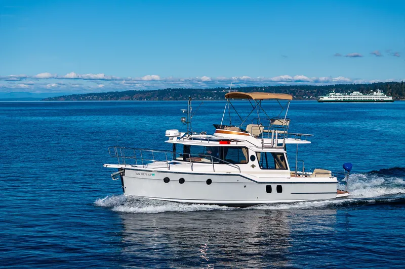 Slide: The Image of 2023 Ranger Tugs R-29 CB cruising on a clear blue lake with distant ferry. - 44