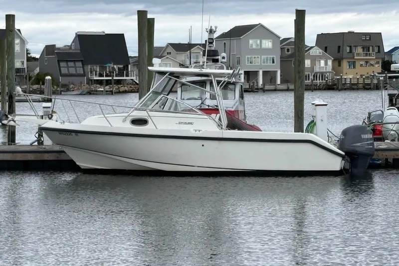 The Image of 1998 Boston Whaler 235 Conquest boat docked in a marina with waterfront homes. - 1