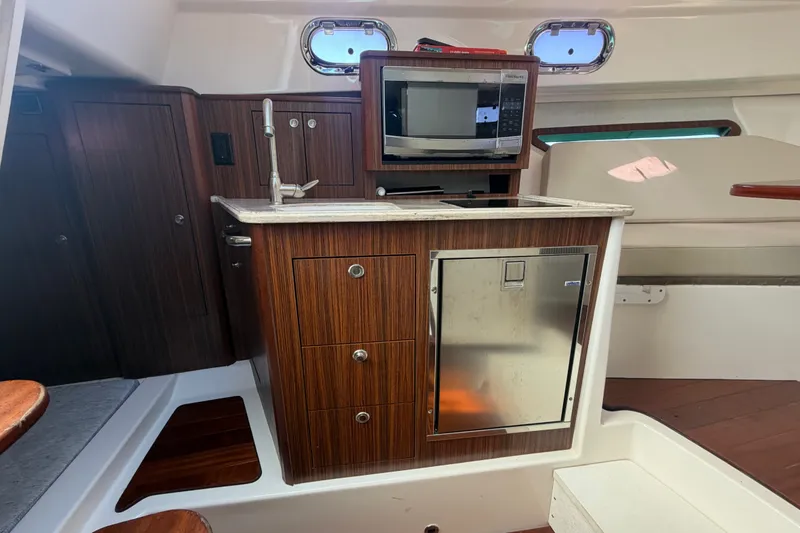 Slide: The Image of 2017 Pursuit OS 325 Offshore boat interior with kitchenette, microwave, and wooden cabinetry. - 43