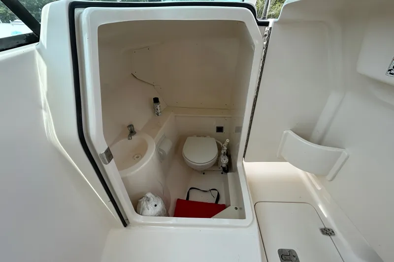 Slide: The Image of Interior of 2012 Pursuit DC 265 Dual Console boat's compact bathroom with toilet and sink. - 16