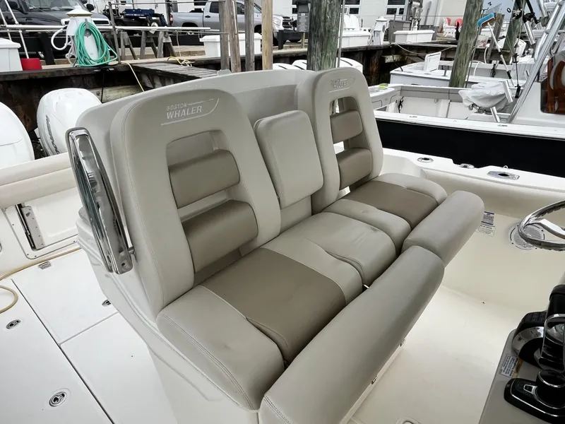 Slide: The Image of 2018 Boston Whaler 330 Outrage boat seating, featuring plush, beige upholstery at a marina. - 19