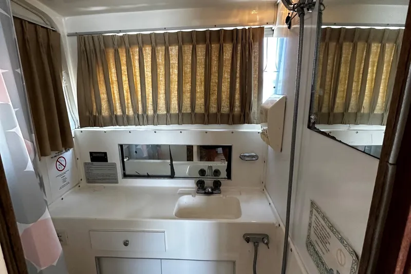 Slide: The Image of 1980 Bertram 33 Sport Fisherman bathroom with sink, mirror, and window with curtains. - 13