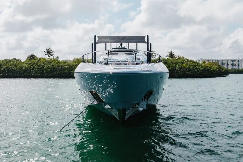 Slide: The Image of Front view of 2024 Mangusta 104 REV yacht on calm water, surrounded by greenery. - 8