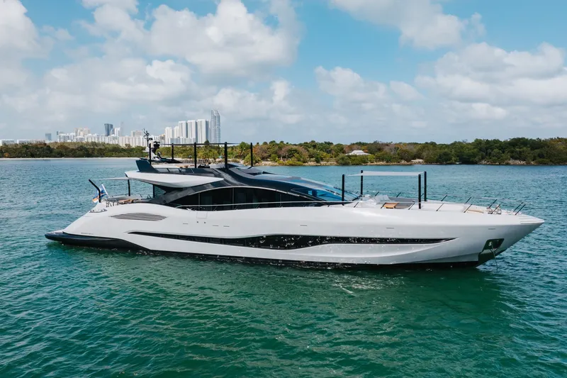 Slide: The Image of 2024 Mangusta 104 REV yacht cruising on a sunny day near a city skyline. - 9