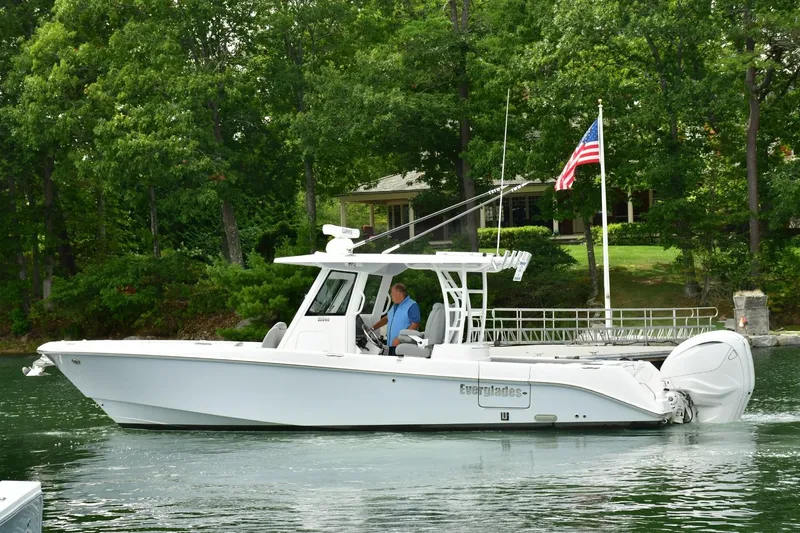 The Image of 2022 Everglades 335 Center Console boat cruising on a serene lake with lush greenery. - 1