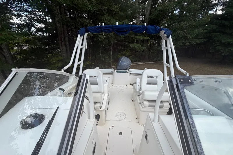 Slide: The Image of 2012 Everglades 230 Dual Console boat interior with seating and canopy, surrounded by trees. - 12