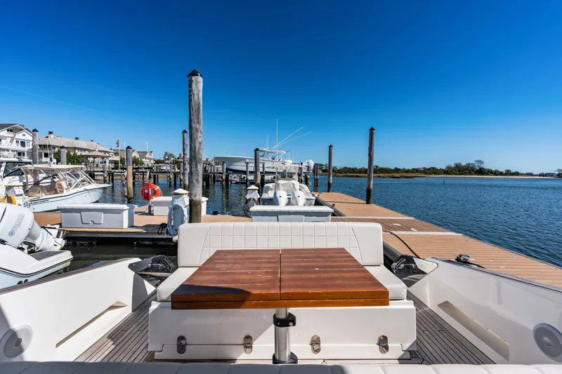 Slide: The Image of The image shows the stern of a 2023 Astondoa 377 Coupe Outboard docked. It features a wooden bench and views of the water and other boats. - 47