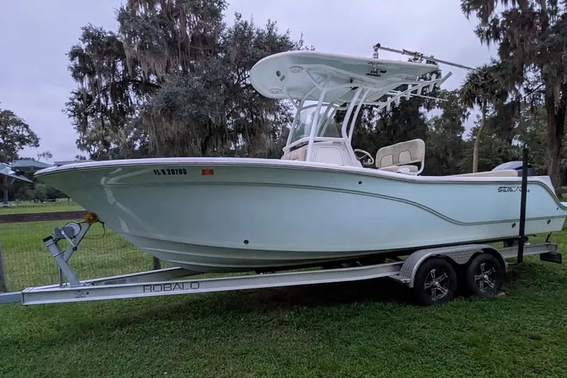 Slide: The Image of 2016 Sea Fox 246 Commander boat on trailer, parked on grass with trees in background. - 2
