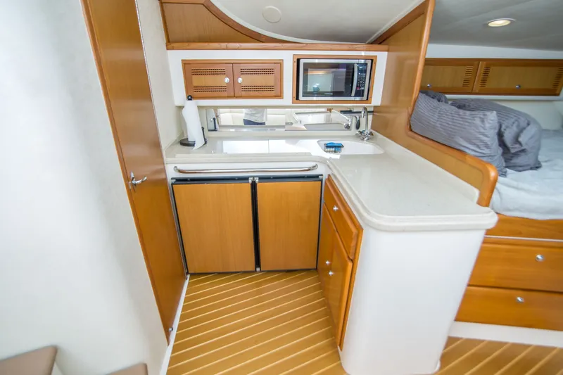 Slide: The Image of 2005 Cabo 35 Express yacht interior with kitchenette, featuring wood cabinetry and modern appliances. - 20