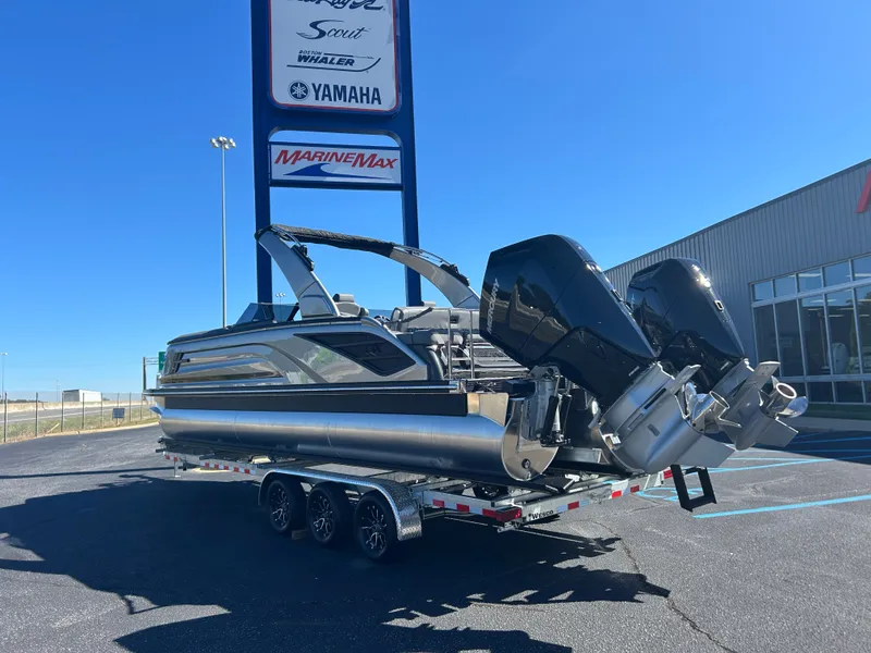 Slide: The Image of A Bennington 27QXSB pontoon boat on a trailer, featuring two outboard motors, parked in a lot. - 4
