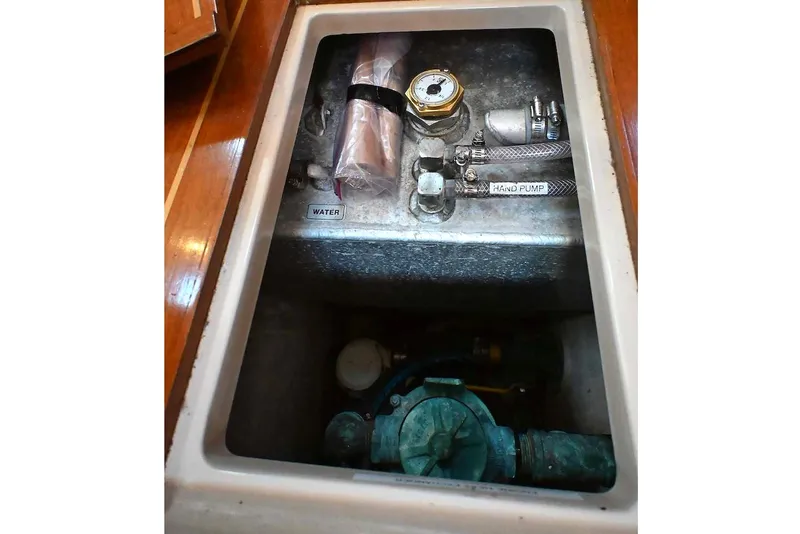 Slide: The Image of Water system compartment in a 2002 Island Packet 350 sailboat, featuring hand pump and gauge. - 63