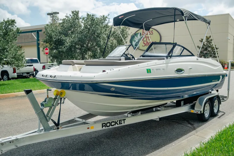 Slide: The Image of 2019 Bayliner 215 Deck Boat on trailer, parked outdoors near a store. - 3