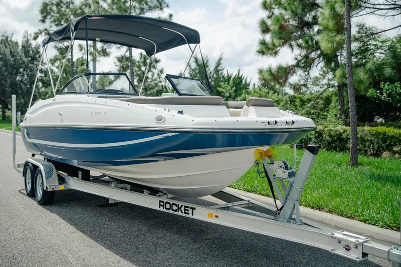 Slide: The Image of 2019 Bayliner 215 Deck Boat on trailer, parked on roadside with lush greenery. - 1