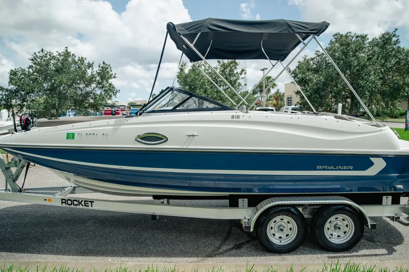 Slide: The Image of 2019 Bayliner 215 Deck Boat on trailer, featuring blue and white design with canopy. - 4