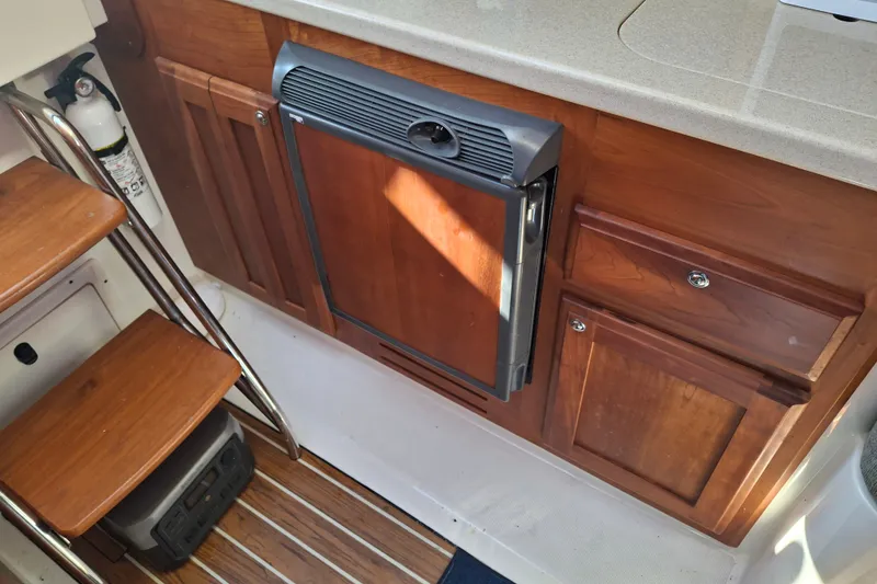 Slide: The Image of Interior of a 2005 Back Cove 26 boat, featuring wooden cabinetry and compact appliances. - 16