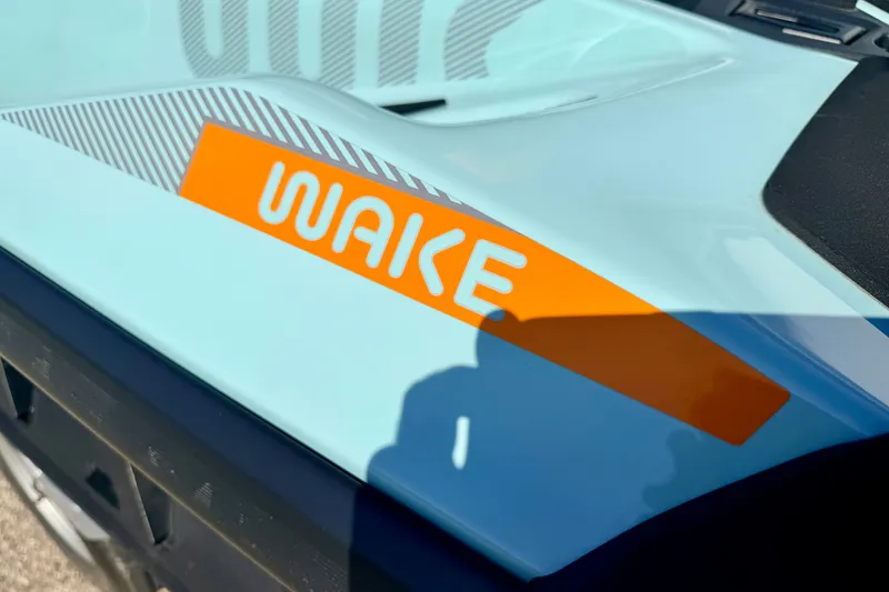 Slide: The Image of 2024 Seadoo WAKE 170 jet ski, close-up of orange "WAKE" decal on light blue body. - 15