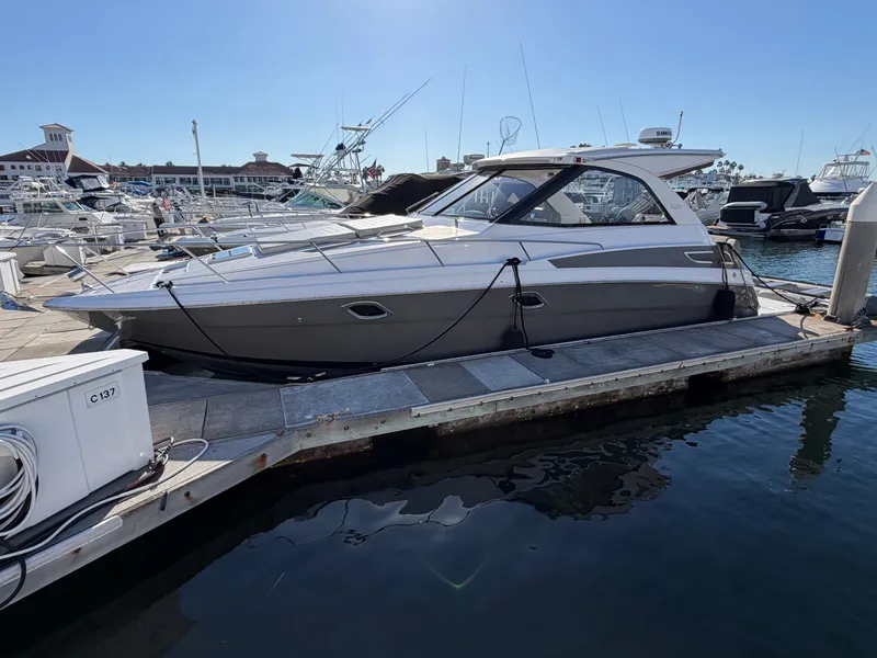 The Image of A 2013 Regal 35 Sport Coupe docked at a sunny marina, surrounded by other boats. - 0