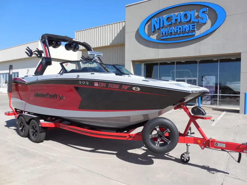 Slide: The Image of A 2023 MasterCraft XStar S boat on a trailer in front of a building with a "Nichols Marine" sign. - 2