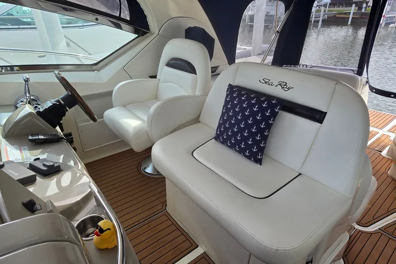 Slide: The Image of 2008 Sea Ray 38 Sundancer cockpit with white seating, anchor-patterned pillow, and wooden flooring. - 13