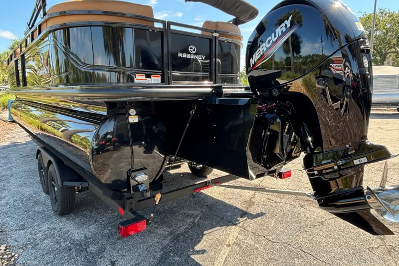 Slide: The Image of 2027 Regency 230 DL3 pontoon boat with Mercury outboard motor, parked on a trailer. - 2