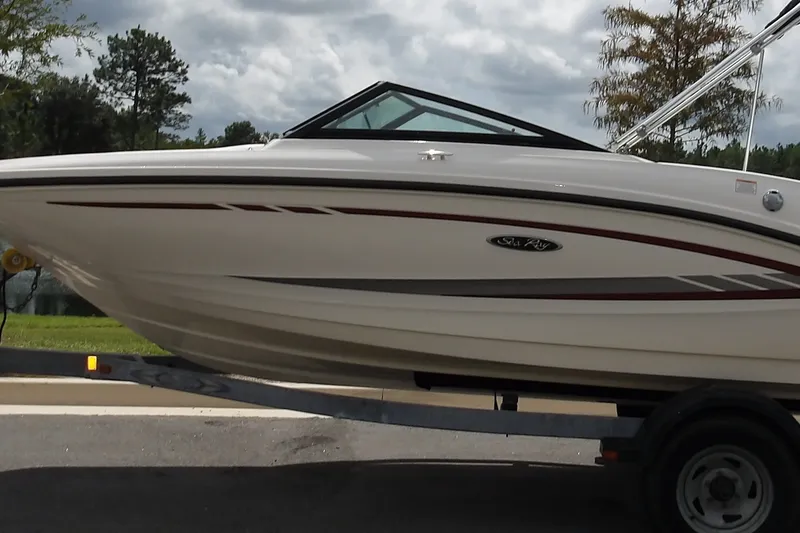 Slide: The Image of 2023 SEA RAY 195 boat on trailer, parked near a scenic lake under a cloudy sky. - 1