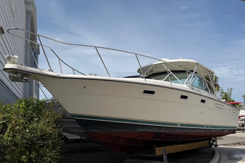 Slide: The Image of A 1996 Pursuit 3100 Offshore boat is on land. It features a white deck and green hull. - 1