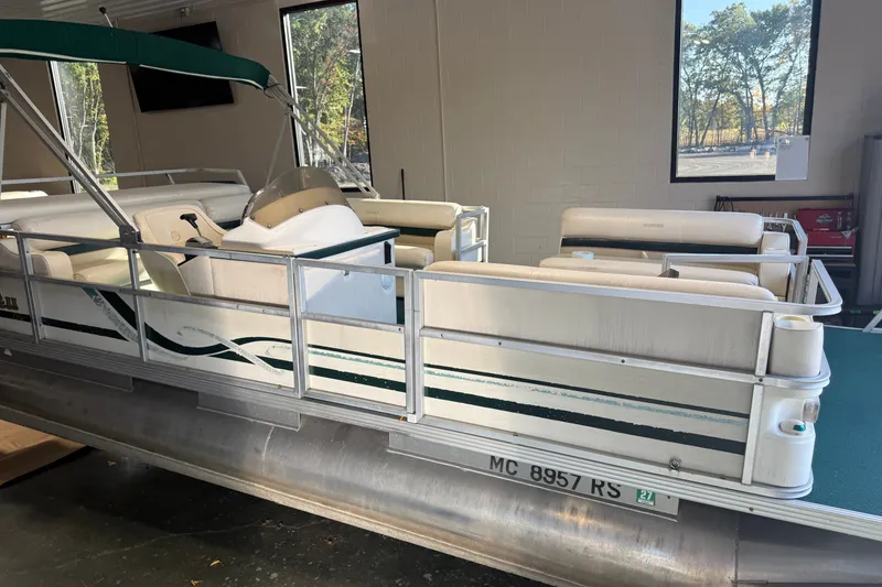 Slide: The Image of 1999 Crest II pontoon boat with green canopy, docked indoors, featuring white seating and railing. - 4