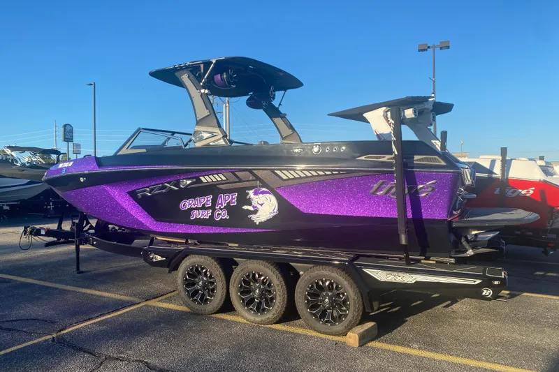 Slide: The Image of 2017 Tigé RZX3 boat with purple "Grape Ape Surf Co." design on trailer in parking lot. - 26