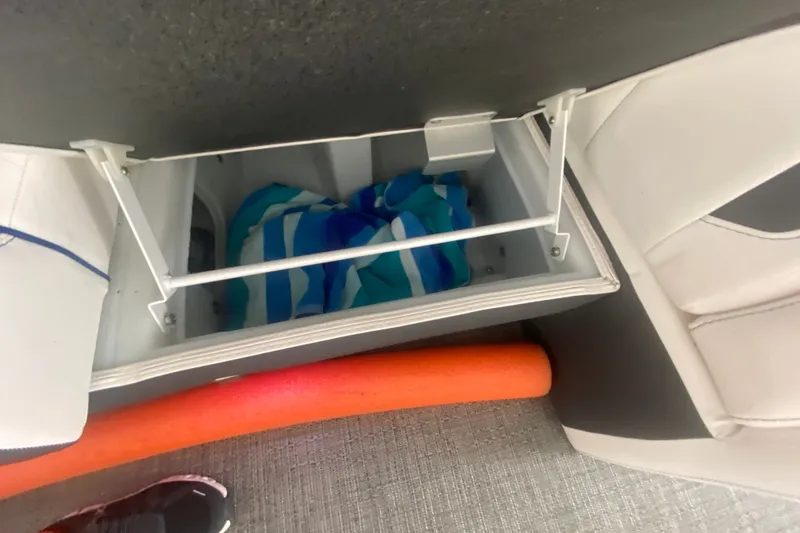 Slide: The Image of Storage compartment in 2024 Barletta Corsa 25U boat with striped towel and orange pool noodle. - 25