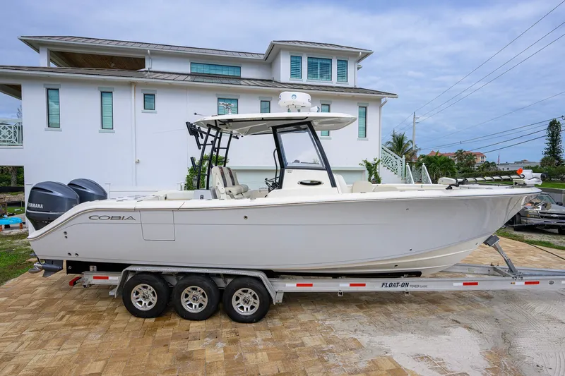 Slide: The Image of 2019 Cobia 301 Center Console boat on trailer, parked near a modern house. - 5