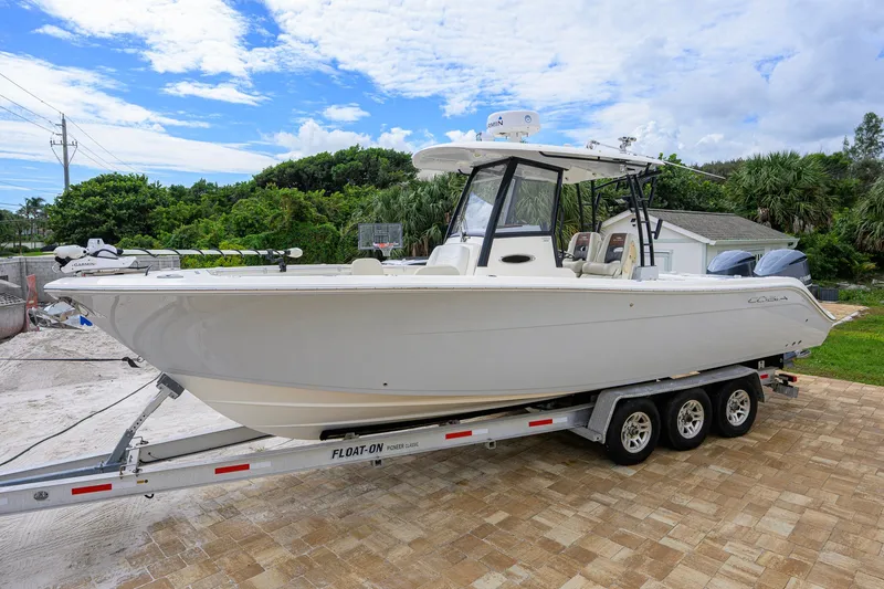 Slide: The Image of 2019 Cobia 301 Center Console boat on trailer, parked outdoors under a blue sky. - 14