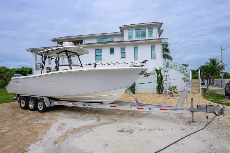 Slide: The Image of 2019 Cobia 301 Center Console boat on trailer, parked in front of a large house. - 6