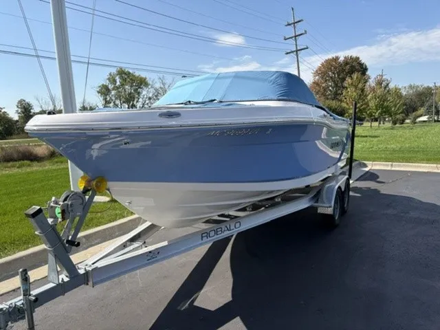 Slide: The Image of A 2023 Robalo R207 Dual Console boat on a trailer, with a blue cover, parked on pavement. - 4