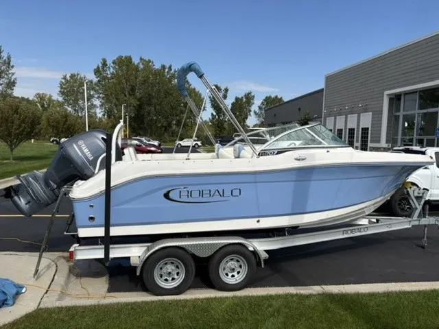 The Image of A 2023 Robalo R207 Dual Console boat on a trailer, featuring a blue hull and outboard motor. - 0