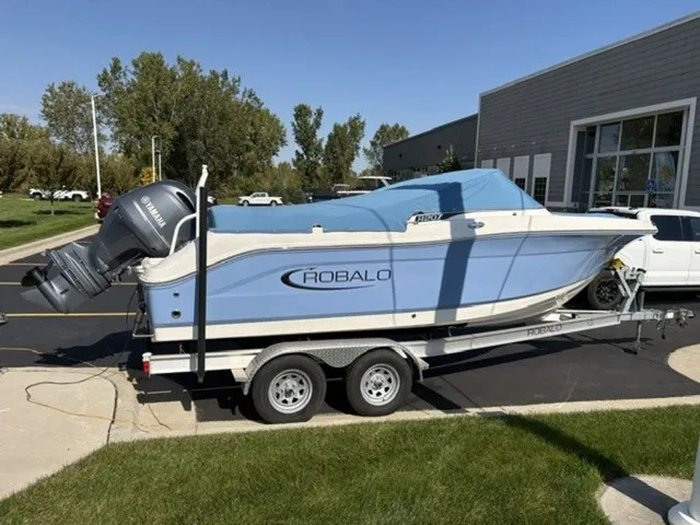 Slide: The Image of A 2023 Robalo R207 Dual Console boat on a trailer, featuring a blue cover and outboard motor. - 2