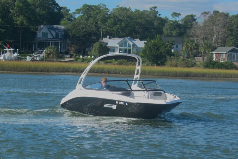 Slide: The Image of 2025 Yamaha Boats AR190 cruising on a scenic waterway near waterfront homes. - 4