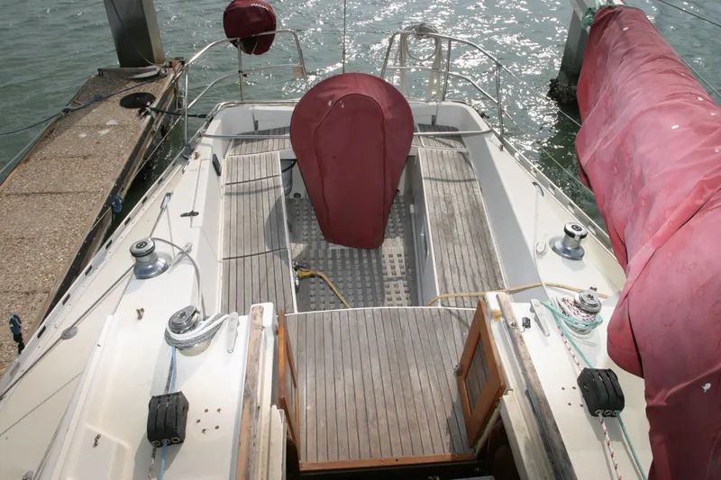Slide: The Image of 1983 Beneteau Idylle 11.50 sailboat docked, featuring a spacious wooden deck and covered equipment. - 10