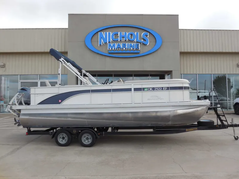 Slide: The Image of A 2019 Bennington 22 SSx APG pontoon boat on a trailer in front of a marine store. - 1