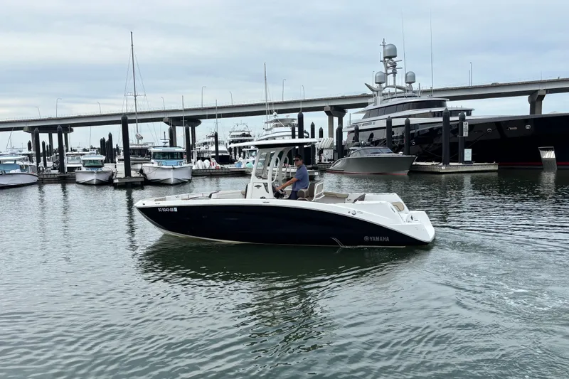 Slide: The Image of 2022 Yamaha Boats 255 FSH Sport E cruising in a marina with yachts and a bridge. - 6