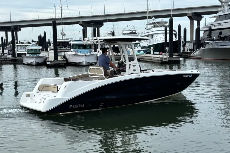 Slide: The Image of 2022 Yamaha Boats 255 FSH Sport E cruising in a marina with docked yachts. - 5