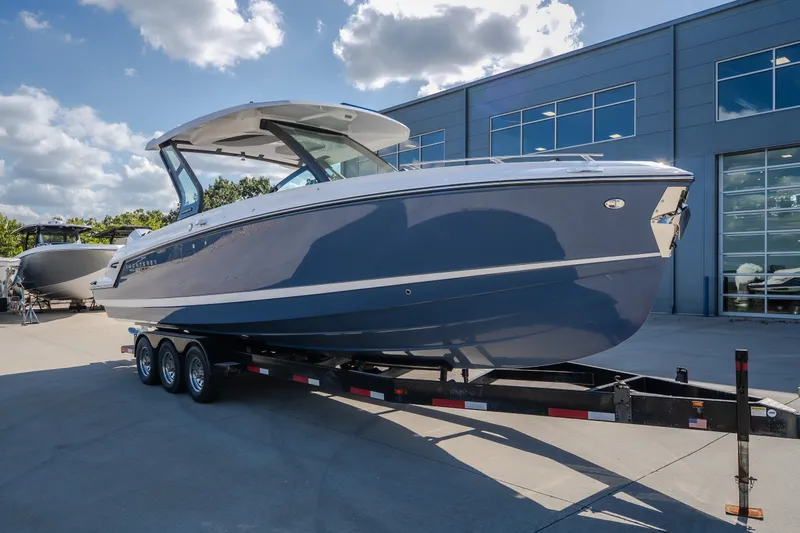 The Image of 2027 Monterey Elite 27 OB boat on trailer, parked outside modern building under blue sky. - 0