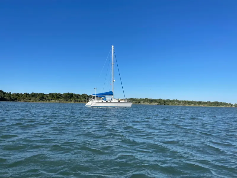 Slide: The Image of A 1990 Jeantot Privilege 39 catamaran sails on calm waters under a clear sky. - 2