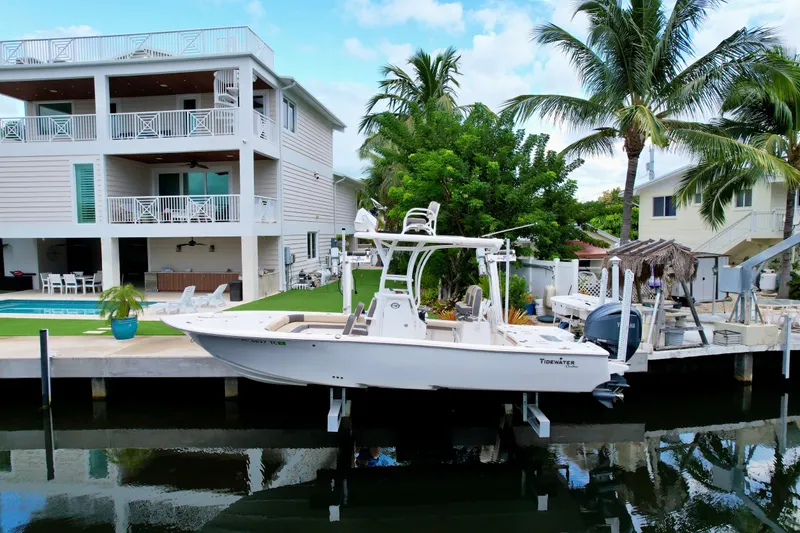The Image of 2021 Tidewater 2500 Carolina Bay boat docked by a waterfront home with palm trees. - 0