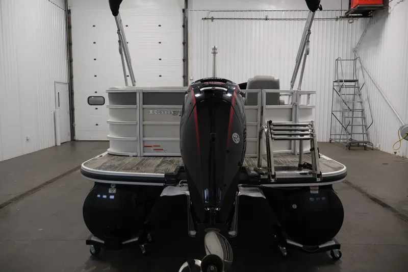 Slide: The Image of 2025 Ranger Reata 220C pontoon boat in a garage, rear view with motor and ladder. - 6