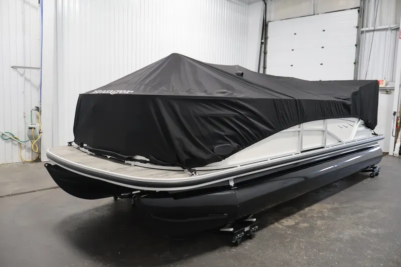 Slide: The Image of 2025 Ranger Reata 220C pontoon boat covered in black tarp, stored indoors. - 42