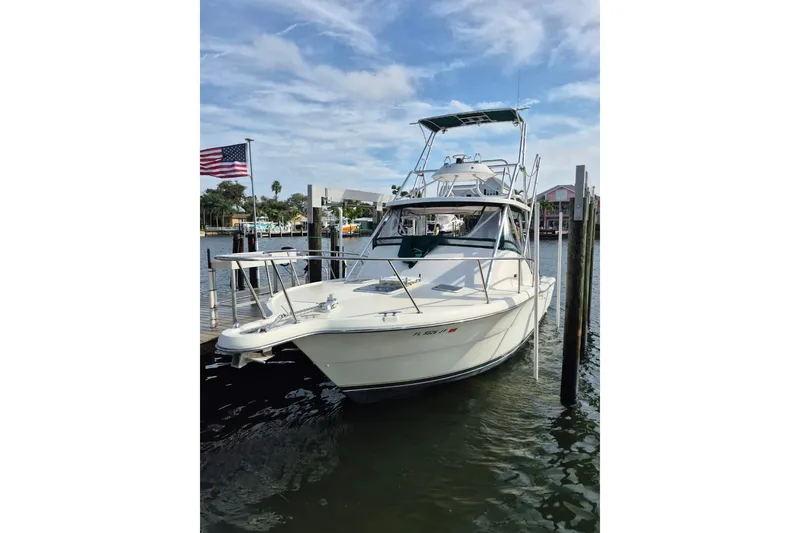 Slide: The Image of 1996 Pursuit 3000 Offshore boat docked, American flag in background, calm waters. - 66