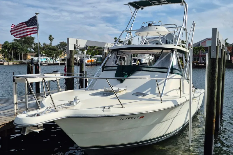 Slide: The Image of 1996 Pursuit 3000 Offshore boat docked, American flag waving, sunny marina setting. - 65