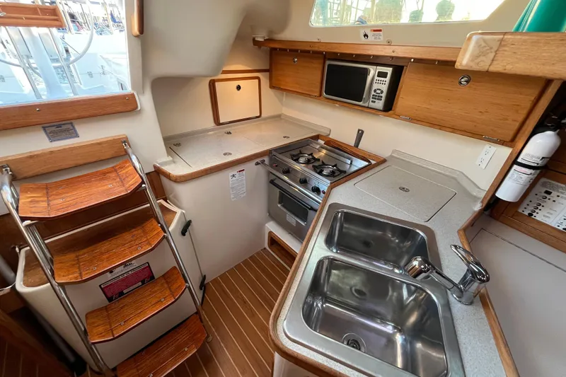 Slide: The Image of Catalina 320 yacht kitchen interior, featuring wooden cabinetry, dual sink, stove, and microwave. - 5