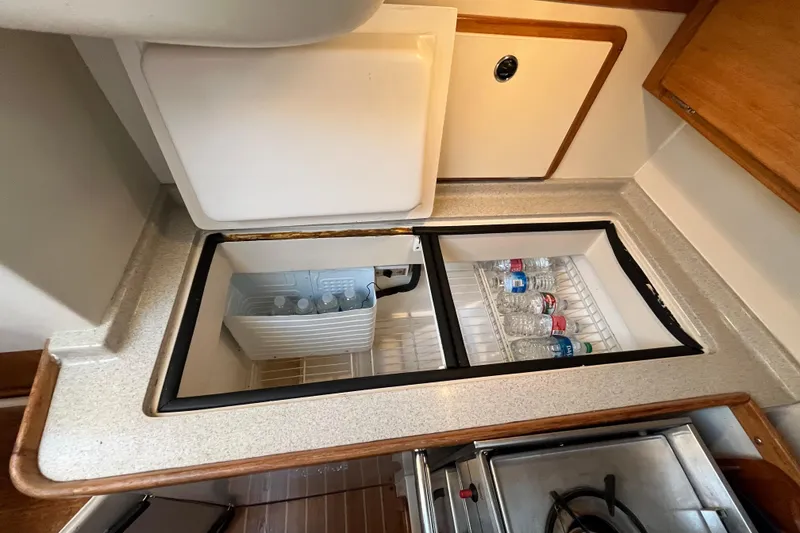 Slide: The Image of 2005 Catalina 320 yacht galley with open fridge, stocked with water bottles. - 10