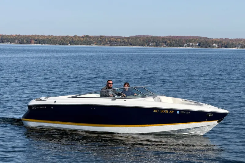 Slide: The Image of 2004 Cobalt 250 boat cruising on a calm lake with scenic forested shoreline. - 0